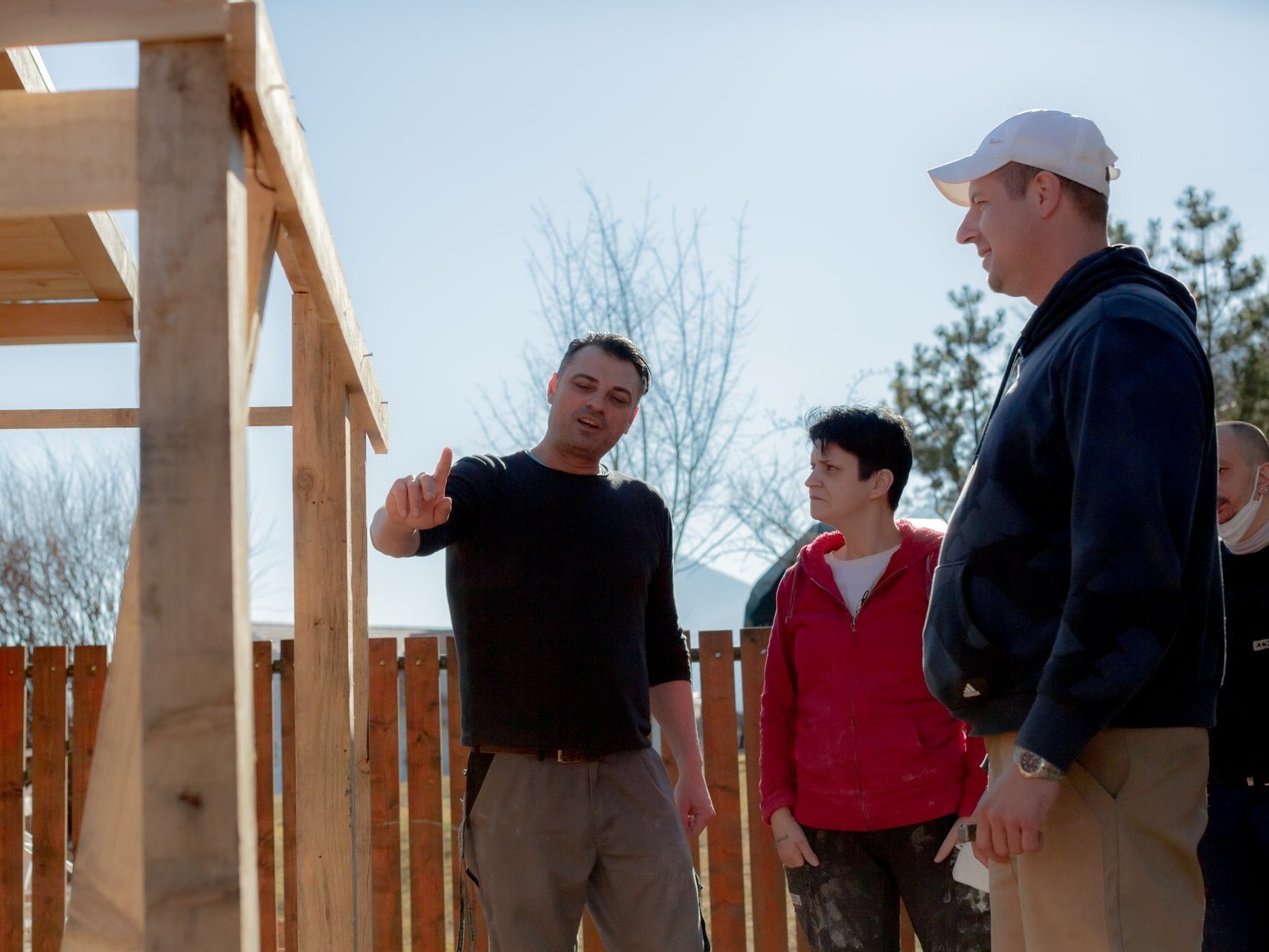 Eine Frau und drei Männer stehen vor einer Holzkonstruktion - ein Mann erklärt