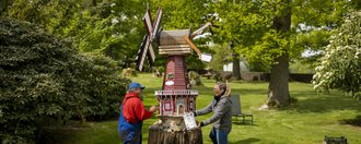 Zwei Menschen bemalen gemeinsam eine Windmühle in einem Garten.