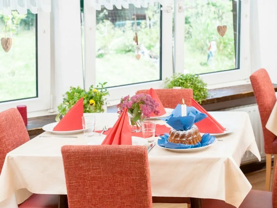 ein Kaffetisch für vier Personen gedeckt mit roten Stühlen und weisser Tischdecke