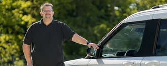 Ein Mitarbeiter des ambulanten Dienstes steht lächelnd neben seinem Dienstfahrzeug.