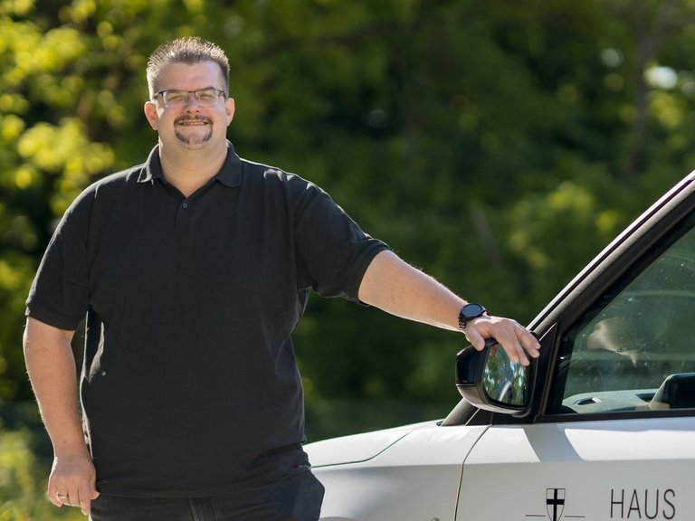 Ein Mitarbeiter des ambulanten Dienstes steht lächelnd neben seinem Dienstfahrzeug.