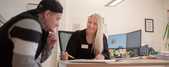 eine nette Mitarbeiterin erklärt einem Besucher etwas anhand eines Schriftstücks