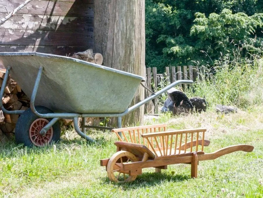 Eine Spielzeug-Schubkarre aus Holz steht vor einer großen Schubkarre aus Metall