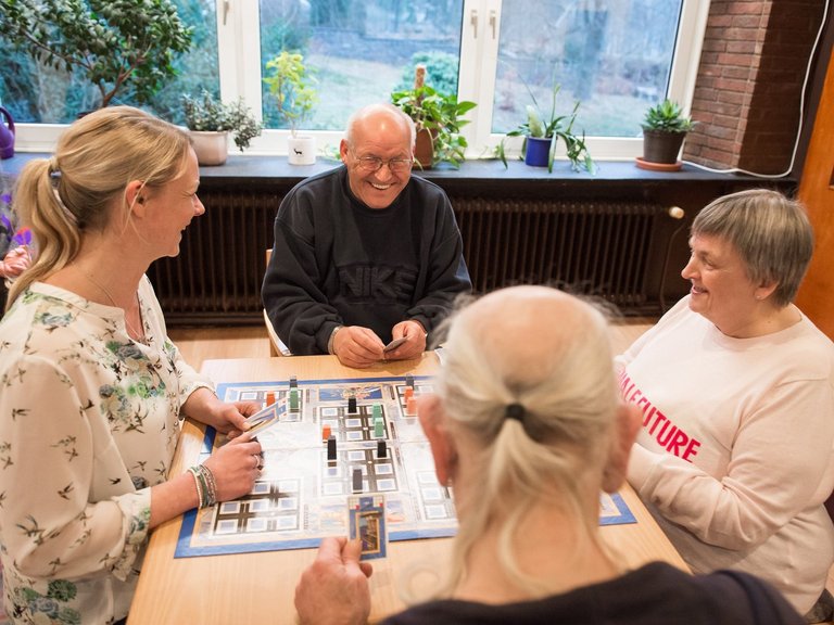 Männer und Frauen spielen ein Brettspiel und lachen dabei