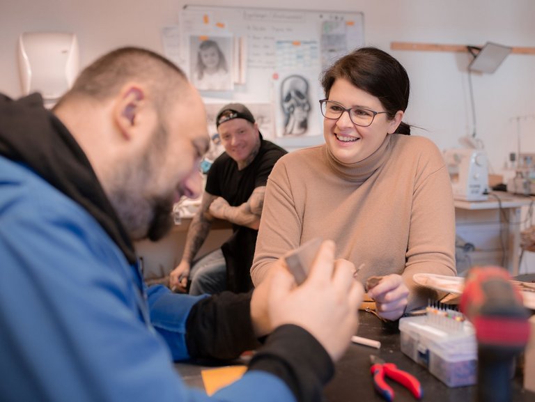 freundliche Mitarbeiterin im Gespräch mit einem Mann, der gerade an etwas in der Werkstatt arbeitet